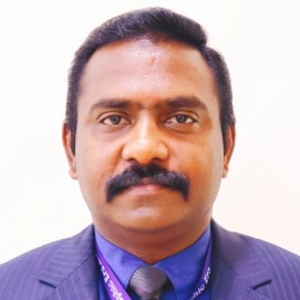Professional head-and-shoulders portrait of a man with a mustache wearing a dark suit, blue shirt, and tie, facing the camera, with a purple lanyard.